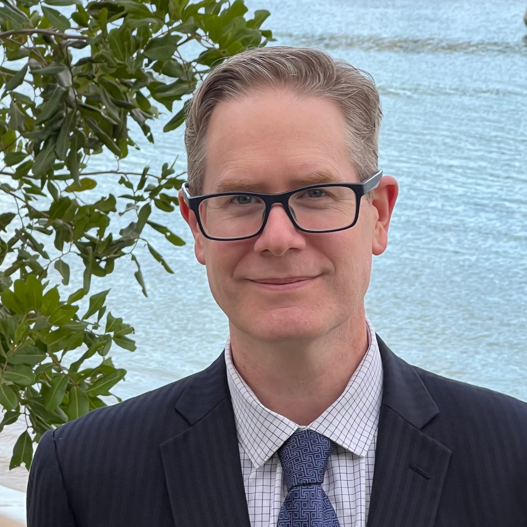 David Kinnane | Banter Speech & Language Man wearing glasses and a suit, standing in front of a bay