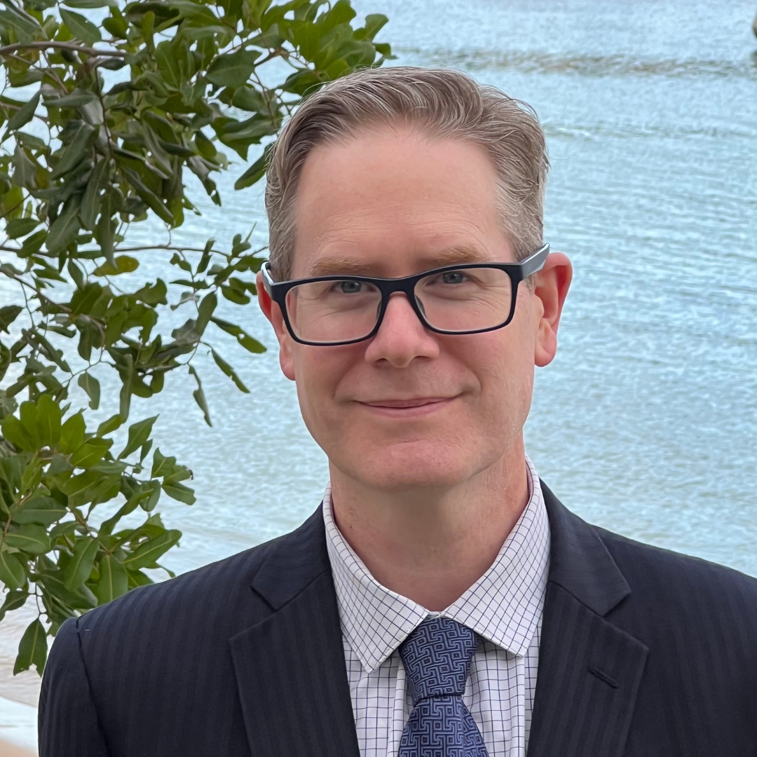 Man wearing glasses and a suit, standing in front of a bay