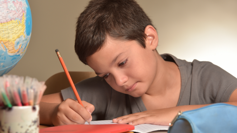 Boy at a table writing with a pencil