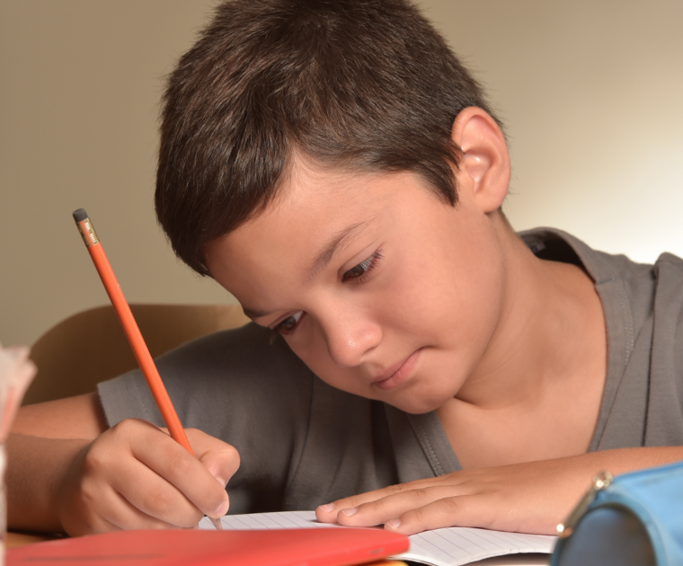 Boy at a table writing with a pencil