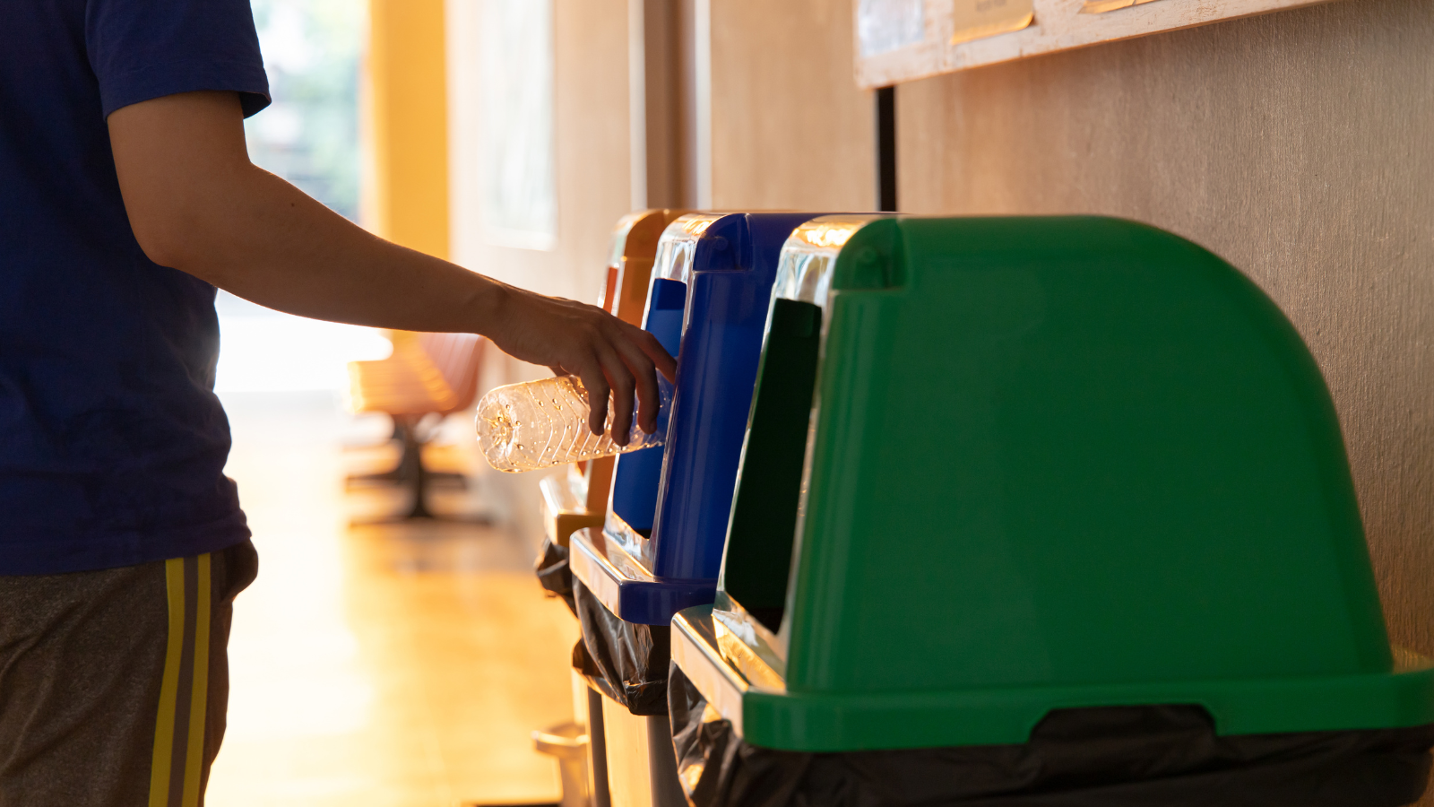 A person placing a clear plastic bottle in a recycling bin