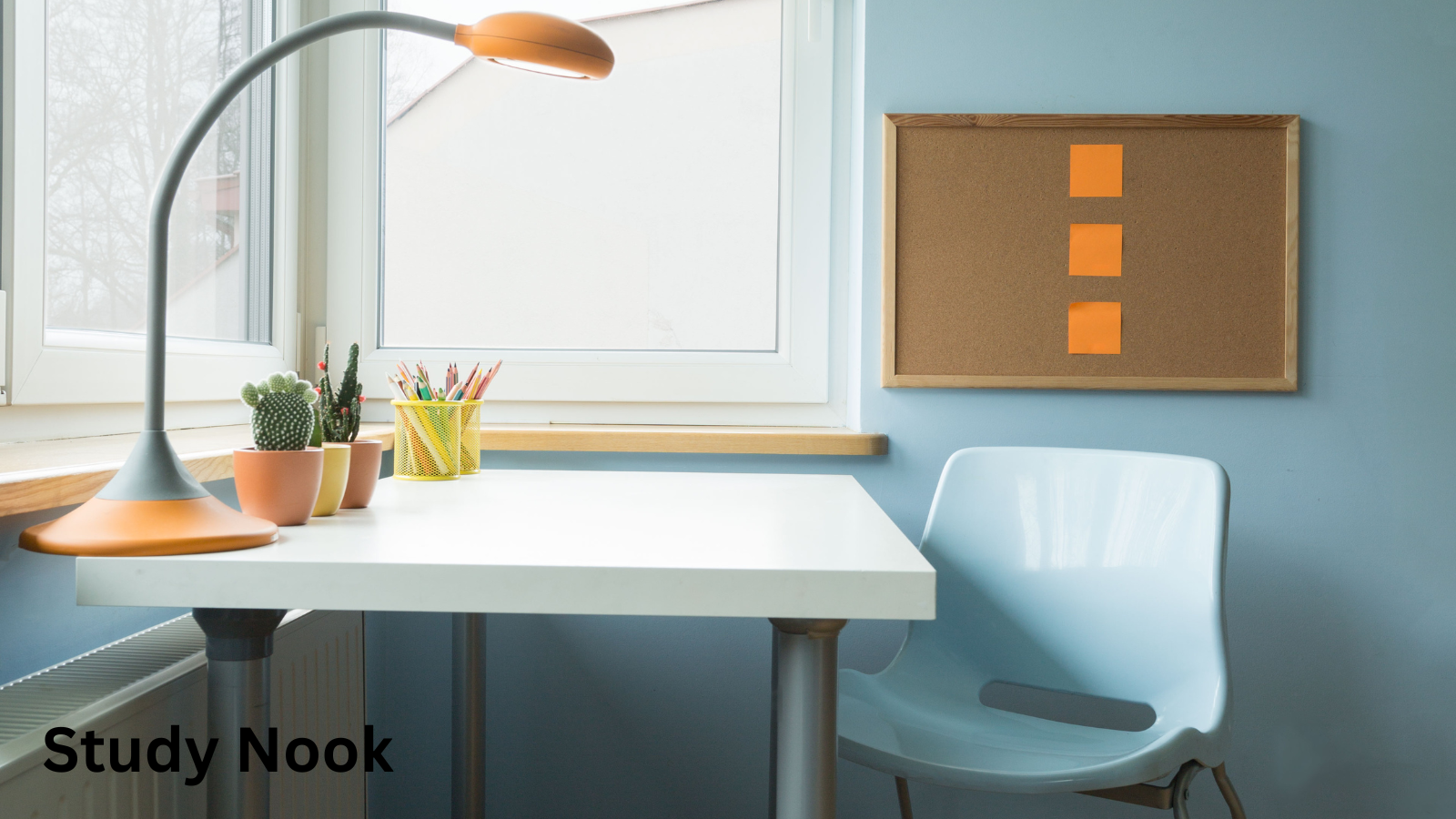 A desk in the corner of a room with an orange lamp, pencils, plants and a blue chair. The desk is underneath two windows and there is a noticeboard on the wall.