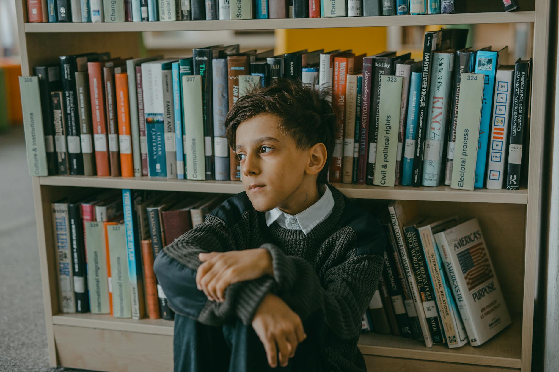 a boy sitting and leaning on a bookcase